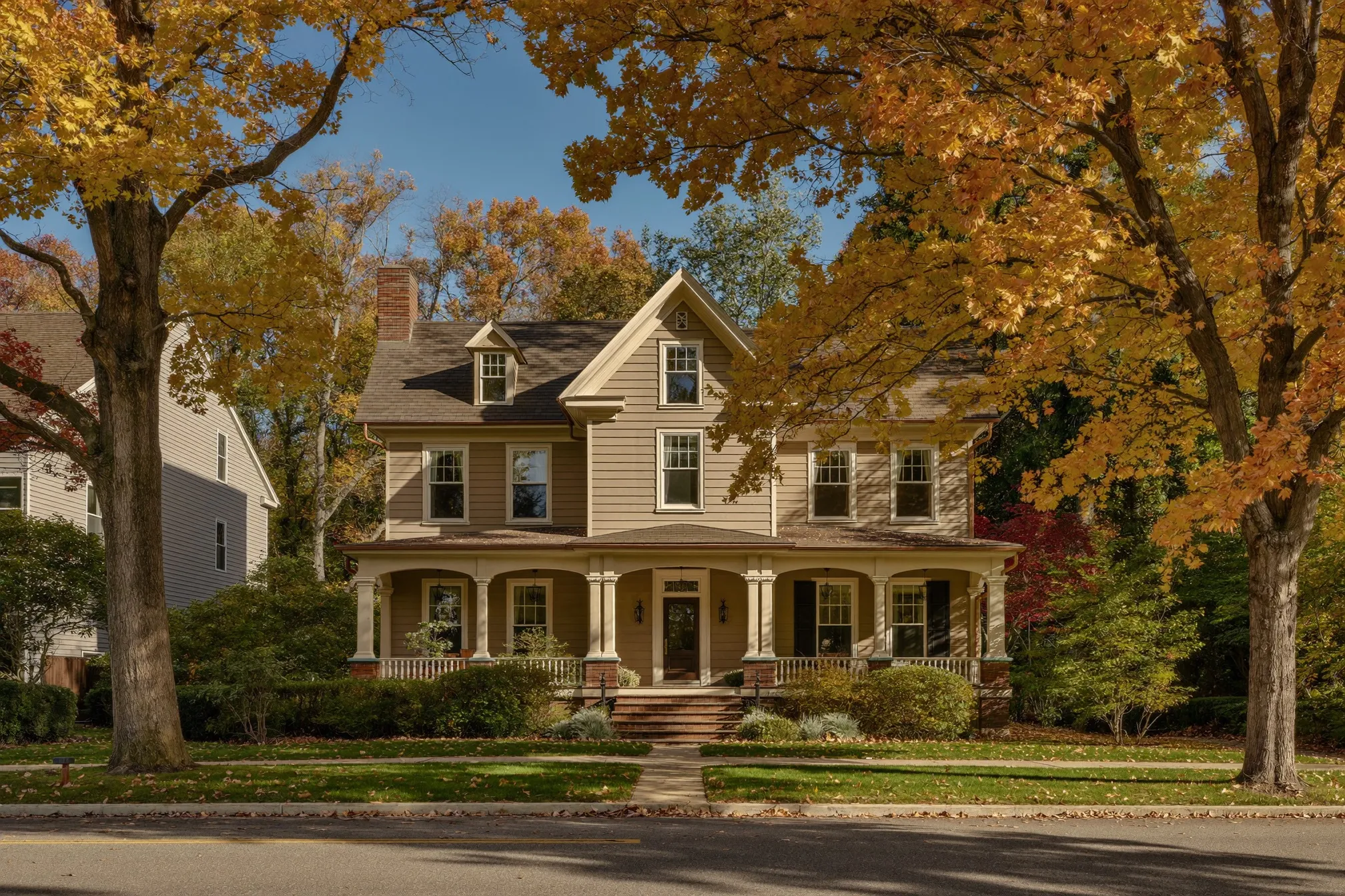 Historic Victorian home with a wraparound porch on a tree-lined Central New York street in autumn